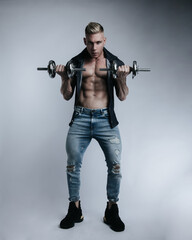 Fototapeta na wymiar Powerful full-length portrait of muscular sexy man in jeans with dumbbells at white background. Handsome fitness male model with gym equipment in studio.
