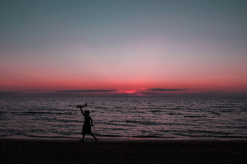Fototapeta premium happy girl running with a kite at sunset outdoors. A child runs with a kite at sunset against the backdrop of the sea. Family vacation. High quality photo.