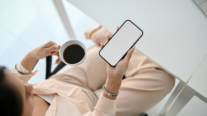 Top view of a professional Asian businesswoman sipping coffee and using her smartphone at her desk