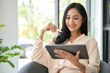 Charming Asian businesswoman using digital tablet, looking for an inspiration on the internet.