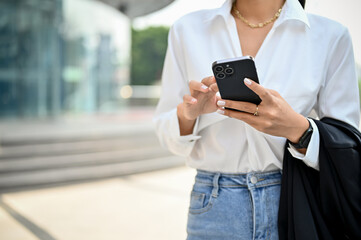 Cropped image of a gorgeous Asian businesswoman using her smartphone while walking on the street