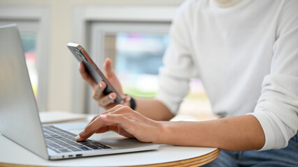 Fototapeta premium Cropped image of a female remote working at the cafe, using laptop and her phone.