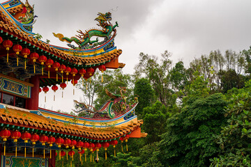 Chinese temple on the background of the jungle. Richly decorated roofs. Sculptures of dragons and hanging red lanterns. Cloudy day. Kuala Lumpur. Malaysia