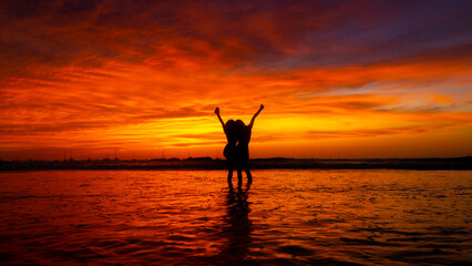 Twilight Silhouette of two women at the beach with arms raised