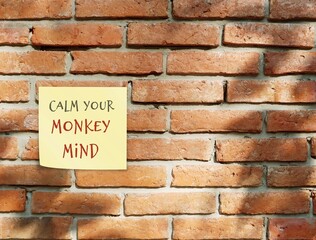 Fototapeta na wymiar Brown brick wall with note written CALM YOUR MONKEY MIND, Buddhism mindfulness practice to control distraction wandering mind which unfocused jumping from thought to thought like naughty monkey