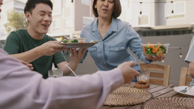 Mom enjoy cooking for family day dining at dine table cozy patio front yard home. Mum passing food serving drink to group four asia people young adult man woman friend fun joy relax warm picnic eating