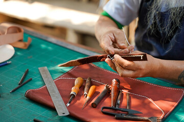 Closeup hand of leather craftsman is carefully to sew a leather belt for a customer., Leather craftsman concept.