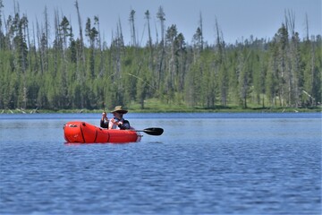 Older, bearded Caucasian man fishing from a red inflatable kayak.  Rod bent with fish on.