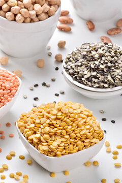 Uncooked toor dal in bowl with multiple legumes and lentils on white background
