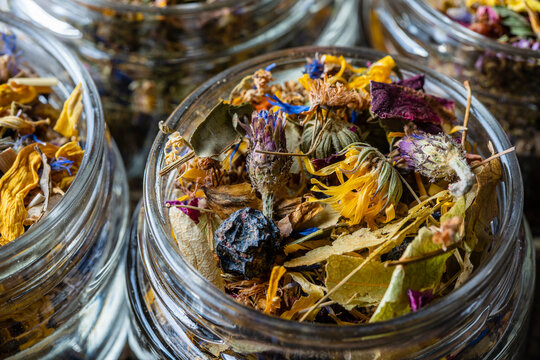 Dry flower and herbal tea leaves in a glass jar on wooden background. Herbal collection of chamomile, cornflower, mint, sea buckthorn, lemongrass, wild rose, dried citrus fruits and apple