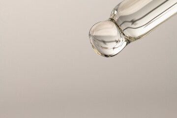 Macro of a glass dropper with essential oil for massage and spa on a gray background with copy space. Beauty procedures, body care.