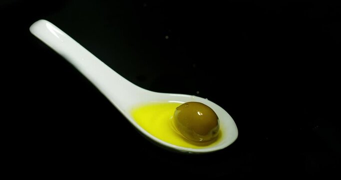 Green Olive, Olea europaea, Falling in a Spoon against Black Background, Slow Motion 4K