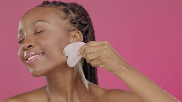 Black woman, face or gua sha in skincare beauty, routine grooming or rose quartz therapy on isolated pink background. Smile, happy or model with stone massage, holistic crystal or facial tool product