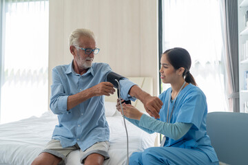 Obraz premium Young asian nurse measuring blood pressure of elderly man.