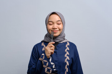 Hungry young Asian Muslim woman with fork in her mouth dreaming about delicious healthy food isolated over white background