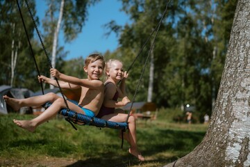 cute little boy and girl having fun on a spiderweb tree swing at playground. Summer vacation in the nature.