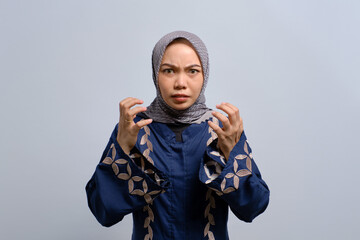 Angry young Asian Muslim woman raising hands and shouting with rage isolated over white background