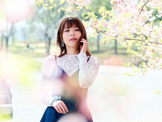 Outdoor portrait of beautiful young Chinese girl posing with blossom cherry tree brunch background in spring garden, beauty, summer, emotion, lifestyle, expression and people concept.