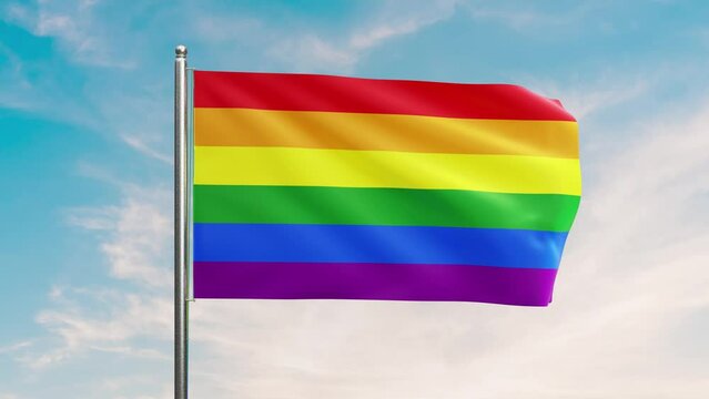 A LGBTQ+ rainbow progress pride flag flaps from a flagpole in a brisk breeze. beautiful Blue sky behind