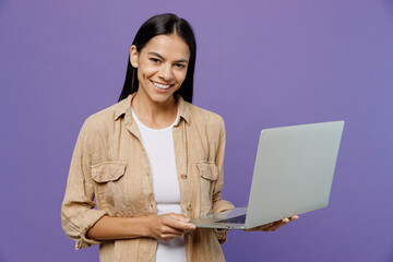 Young smiling happy fun cheerful cool IT latin woman wears light shirt casual clothes hold use work on laptop pc computer isolated on plain pastel purple color background studio. Lifestyle concept. - obrazy, fototapety, plakaty