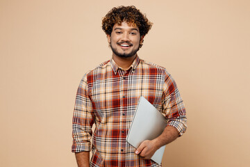 Side view young Indian IT man wear brown shirt casual clothes hold closed laptop pc computer...