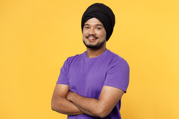 Happy devotee Sikh Indian man ties his traditional turban dastar wear purple t-shirt hold hands crossed folded look camera isolated on plain yellow background studio portrait People lifestyle concept