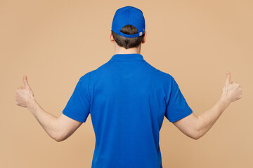 Back rear view professional delivery guy employee man wear blue cap t-shirt uniform workwear work as dealer courier showing thumb up like gesture isolated on plain beige background. Service concept.