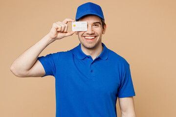 Delivery guy employee man wear blue cap t-shirt uniform workwear work dealer courier hold in hand cover eye with mock up of credit bank card isolated on plain light beige background Service concept.
