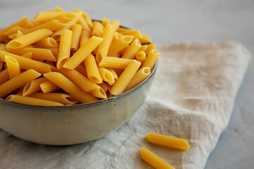 Raw Organic Penne Pasta in a Bowl on a gray background, side view. Close-up.