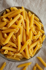 Raw Organic Penne Pasta in a Bowl on a gray background, top view. Flat lay, overhead, from above.