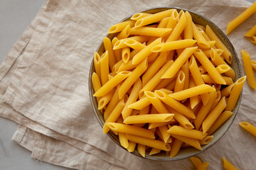 Raw Organic Penne Pasta in a Bowl on a gray background, top view. Flat lay, overhead, from above. Copy space.