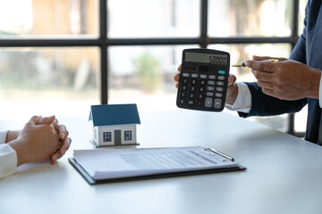 Young Asian businessman or insurance salesman explaining details of sales contract and calculating numbers with calculator to client before signing agreement Home relocation or house hunting concept.