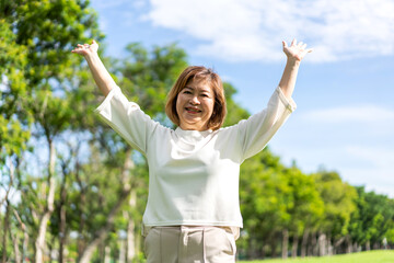 Fototapeta na wymiar Portrait of happy senior old adult elderly asia women smiling standing and stretch her arms relax and enjoy with nature feeling breath fresh clean air in green park.Healthcare