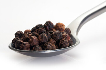 black pepper in a spoon on white background