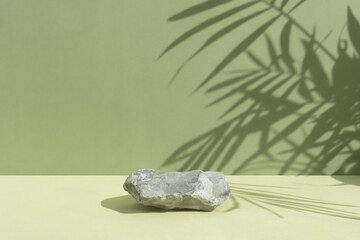 An empty podium made of gray stone on a green background with a shadow of tropical leaves. Scene for the promotion of products, beauty, natural eco-cosmetics. Showcase, display case.