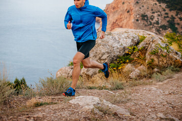 male runner running on mountain trail along sea