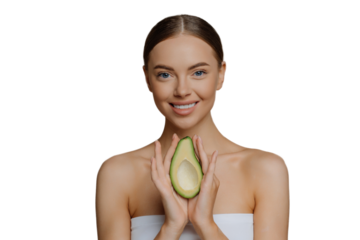 Beauty and personal care concept. Smiling calm European woman with combed hair holds avocado as recommendation for nourishing face mask wrapped in bath towel isolated over beige studio background