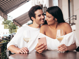 Smiling beautiful woman and her handsome boyfriend. Happy cheerful family. Sexy couple cheering with glasses of red wine at their date in restaurant. Drinking alcohol at veranda cafe. Using phone