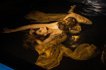 Young beautiful caucasian woman in golden dress in water