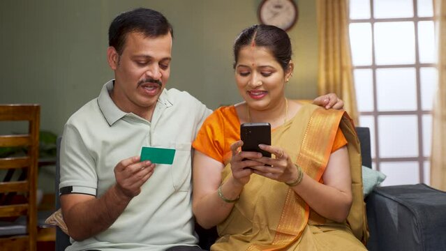 Happy middle aged couple making online payment using credit on mobile phone at home - concept of online shopping, secure transaction and banking or finance