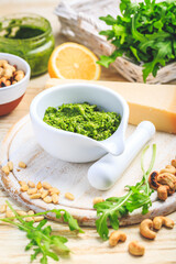Homemade arugula pesto with ingredients on wooden background