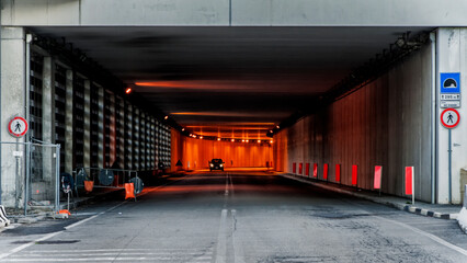 Strada, autostrada, tunnel, sottopasso con automobile solitaria, fari accesi nel buio. - obrazy, fototapety, plakaty