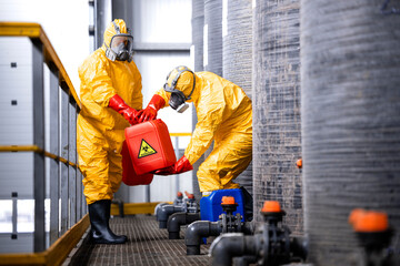 Factory workers carefully handling toxic and dangerous biohazardous waste in chemicals factory. - obrazy, fototapety, plakaty