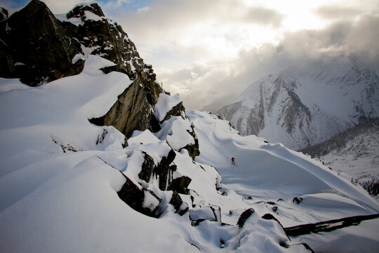 A backcountry skier skins below the ridgeline on a cloudy winter day.
