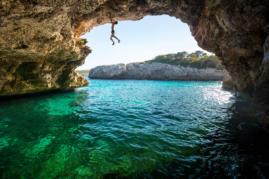 Rock climber climbing across natural arch, Cala Varques, Manacor, Mallorca, Spain