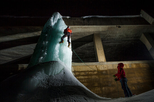 Two boys climbing an icefall near a tunnel on Simplon Pass road by night. Simplon, Valais, Switzerland.