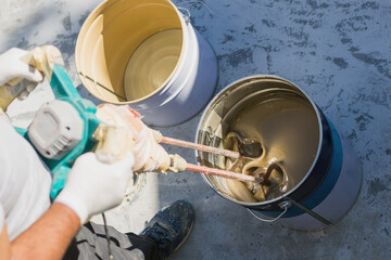Worker mixing yellow epoxy resin with the mixer in a bucket