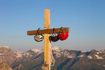 Climbing helmets are dangling on the summit cross of the Eiger Rostock in the Swiss Alps of Grindelwald in Bernese Oberland.