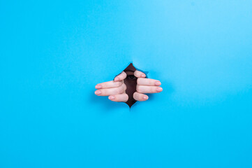 Female hands sticking out through a hole on a blue background. 