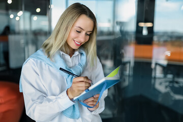 Blonde smiling woman making notes into a notebook